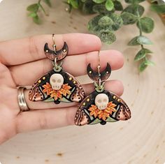 These unique earrings feature a pair of delicate, handcrafted moths, each with a captivating black base and a touch of shimmering bronze pigment. For a touch of autumnal charm, tiny leaves and a miniature skull have been carefully incorporated into the design. These earrings are perfect for adding a touch of whimsy and gothic elegance to any outfit. Polymer clay is a very resistant and lightweight material so you can feel comfortable wearing them from dusk till dawn!  Each design is made with care and love for you to enjoy. They are handmade so expect small imperfections like part of my fingerprints or brush strokes.  No two earrings are exactly alike, which makes each pair unique. The colors you see in the pictures are very accurate to the earrings, but it may be slightly different depend Halloween Earrings Polymer Clay, Skull Moth, Moth Earrings, From Dusk Till Dawn, Gothic Elegance, Dusk Till Dawn, Black Skull, Earrings Halloween, Black Skulls