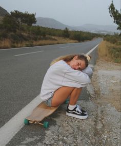 a young woman sitting on the side of a road with her skateboard in front of her