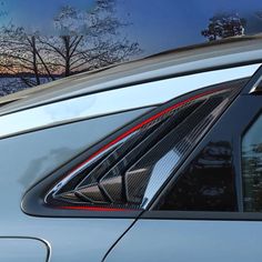 the reflection of trees in the rear window of a silver car with red stripes on it