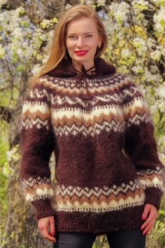 a woman wearing a brown and white sweater standing in front of some trees with flowers