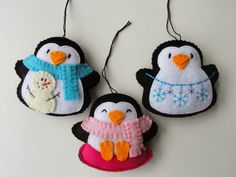 three felt penguin ornaments hanging from strings on a white surface with snowflakes in the background