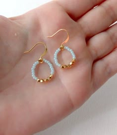 a hand holding two pairs of gold and white beaded earrings on it's palm