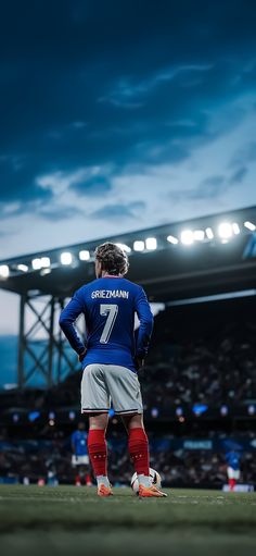 a soccer player stands on the field in front of an empty stadium with his back to the camera