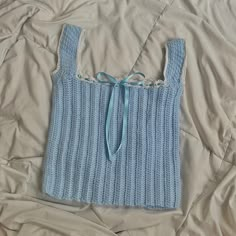 a blue knitted sweater with a tie on top of a white bed coverlet