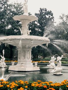 the fountain is surrounded by orange flowers and water spouting from it's sides