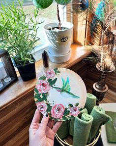 a person holding a plate with flowers painted on it next to potted plants and other items