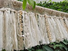 several white laces hanging from a tree in front of some bushes and trees with green leaves