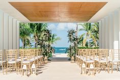 an outdoor wedding setup with chairs and tables set up in front of the ocean, surrounded by palm trees