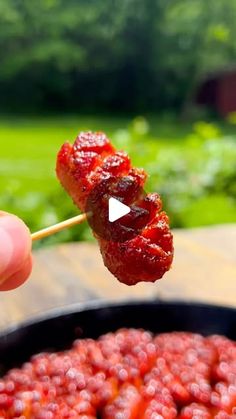 a person holding a skewer of food in front of a bowl full of strawberries