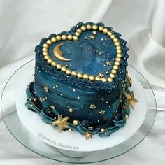 a blue cake with gold stars and a heart shaped decoration on the top is sitting on a plate