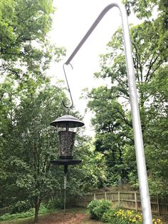 a bird feeder hanging from the side of a metal pole next to trees and flowers