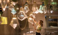 a woman standing in front of a chandelier filled with hanging lights and glass vases