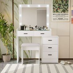 a white vanity with lighted mirror and stool next to potted plant on the floor