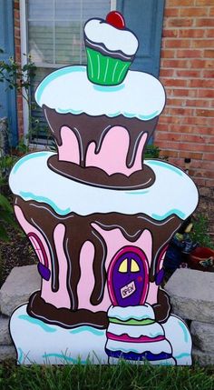 a cardboard cake that is sitting on the ground in front of a brick building with a cupcake on top