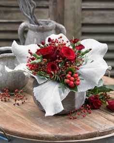 a bouquet of red flowers sitting on top of a wooden table next to a vase