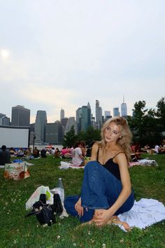 a woman sitting on the grass in front of a city skyline