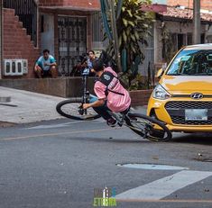 a person riding a bike in front of a yellow car