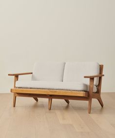 a wooden couch sitting on top of a hard wood floor next to a white wall