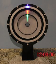 a black and white clock on top of a table next to a wall with a light coming from it