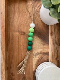 a green and white beaded necklace on a wooden tray next to a potted plant