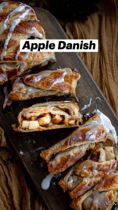 an apple danish with icing on a wooden board next to some apples and cinnamon