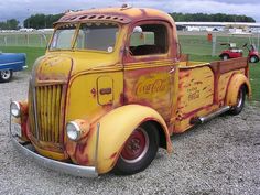 an old yellow coca cola truck parked on gravel