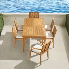 a wooden table and chairs sitting on top of a cement floor next to the ocean