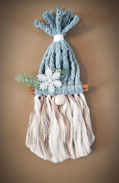 a knitted hat with white flowers and green leaves hanging from a wooden hook on a wall