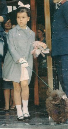 an old photo of a young boy holding a dog on a leash while people look on