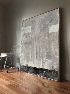 a large painting on the wall next to a chair and table in an empty room