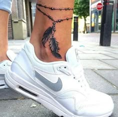 a woman's foot with a feather tattoo on it and a chain attached to the ankle