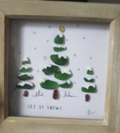 a wooden frame with some green and white rocks in the shape of trees on it