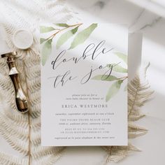 the wedding stationery is laid out on top of a white table cloth with greenery