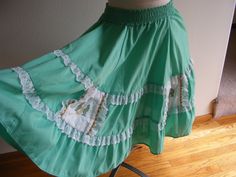 "This is a very cute 1960s vintage green cotton blend square dance full circle skirt. The skirt is made of a nice cotton and poly blend fabric with white lace ruffles and square cotton eyelet detail side pockets trimmed in gold rickrack. It has small, embroidered cactus and horseshoes on the white eyelet detail pockets. It slips on over the head with a wide elastic waist band and has no closures or fasteners. It was made by Pete Bettina, USA and the older size tag states size small. The measurements are as follows: Elastic Waist Band: 2\" wide Waist: 26\" relaxed to 29.5\" stretched Hips: Full Length: 23\" Condition: Very good condition with no obvious flaws or defects to note." Green Full Skirt With Ruffles, Vintage Green Tiered Skirt, Green Full Cotton Skirt, Fitted Green Petticoat For Spring, Retro Cotton Skirt With Ruffles, Embroidered Cactus, Square Dance, Full Circle Skirt, Green Square