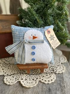 a small snowman pillow sitting on top of a wooden table next to a potted tree