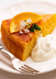 a piece of cake on a white plate with whipped cream and orange wedges next to it