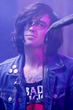 a young man with long hair and piercings standing in front of a microphone on stage