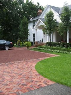 a black car is parked in front of a white house with red brick driveway and landscaping