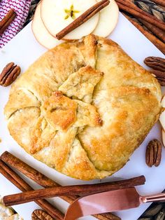 an apple pie is on a white plate with cinnamon sticks, apples and pecans