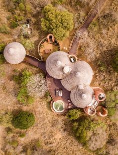 an aerial view of some buildings in the middle of trees and dirt area with several umbrellas on top