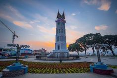 a large clock tower sitting in the middle of a park with lots of flowers around it