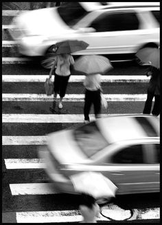 black and white photograph of people crossing the street with umbrellas