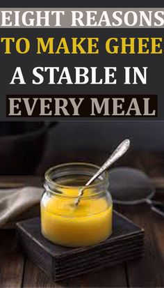 a glass jar filled with yellow liquid sitting on top of a wooden table next to a spoon