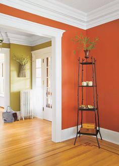 an empty room with orange walls and wooden flooring in the center, along with a plant on top of a shelf