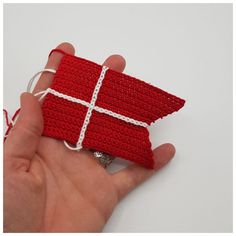 a hand is holding a red piece of crocheted material with white stitching