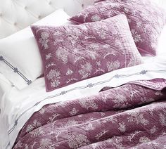 a bed with purple comforters and pillows on it