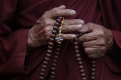 an old man wearing a beaded necklace and holding a wooden rosary in his hands