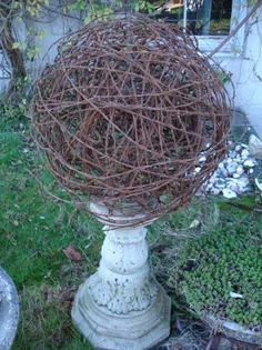 a ball made out of twigs sitting on top of a white pedestal in the grass