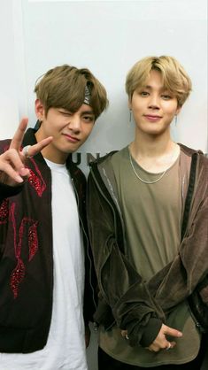 two young men standing next to each other in front of a white wall and pointing at the camera