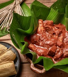 some food is in a bowl on a table with green leaves and other foods around it